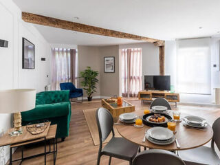 Modern living room and dining area with a set table, exposed wooden beams, and contemporary decor.