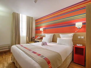 A cheerful bedroom with a colorful striped wall behind a bed with crisp white linen