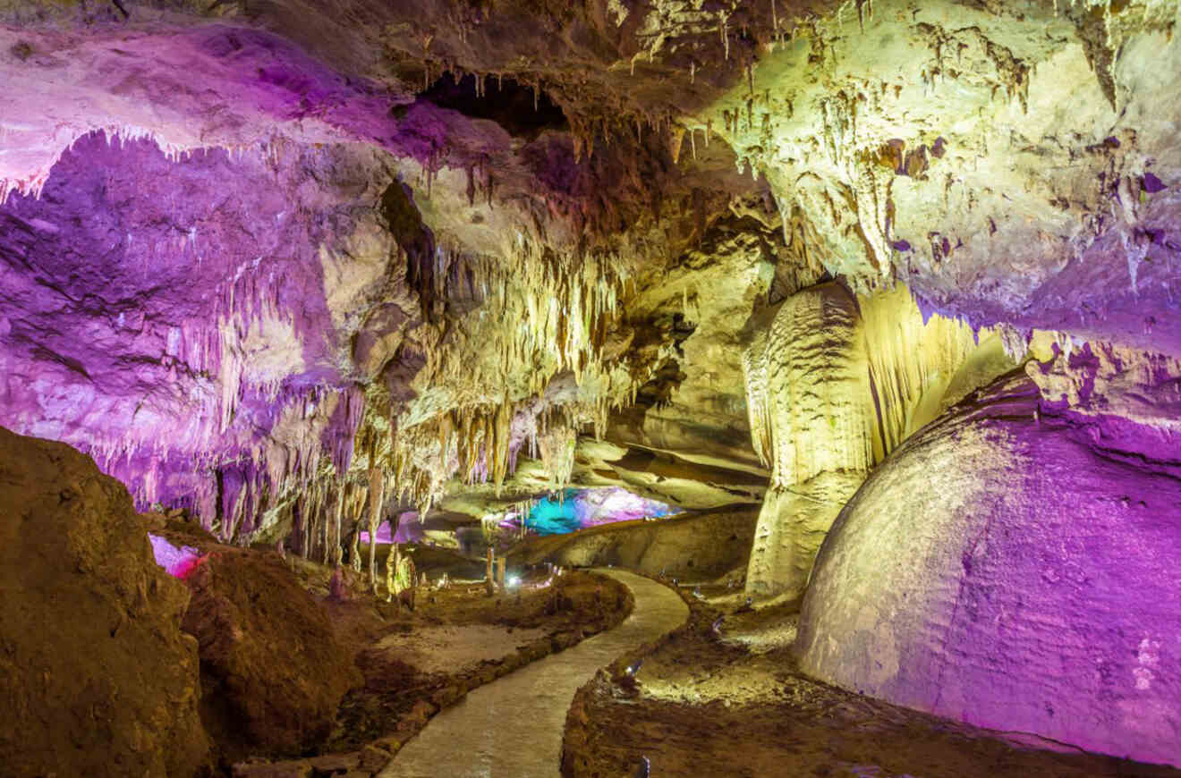 The otherworldly interior of Prometheus Cave, lit with purple lights that cast an ethereal glow over the stalactites and stalagmites, with a smooth pathway inviting exploration