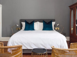 Elegant bedroom featuring a large bed with white linen, teal pillows, and reading lights