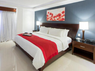 A modern bedroom with a large bed, crisp white linens, and a striking red throw, accented by a vibrant red and white artwork.