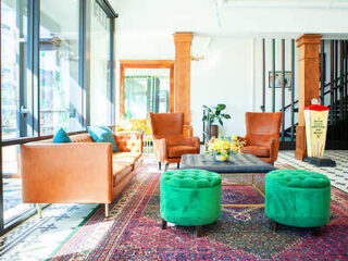 Bright and airy hotel lobby with eclectic seating including orange leather chairs and green velvet ottomans on a colorful area rug