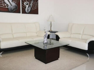 A sleek living room with white leather couches, glass center table, and musical instruments paintings