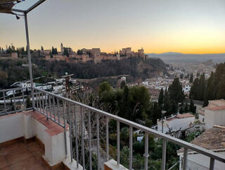 View from a balcony overlooking the alhambra and the city of granada at sunset, with a clear sky and ornate railing in the foreground.