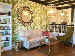 A living room with a tropical-themed wallpaper and tufted cream sofa