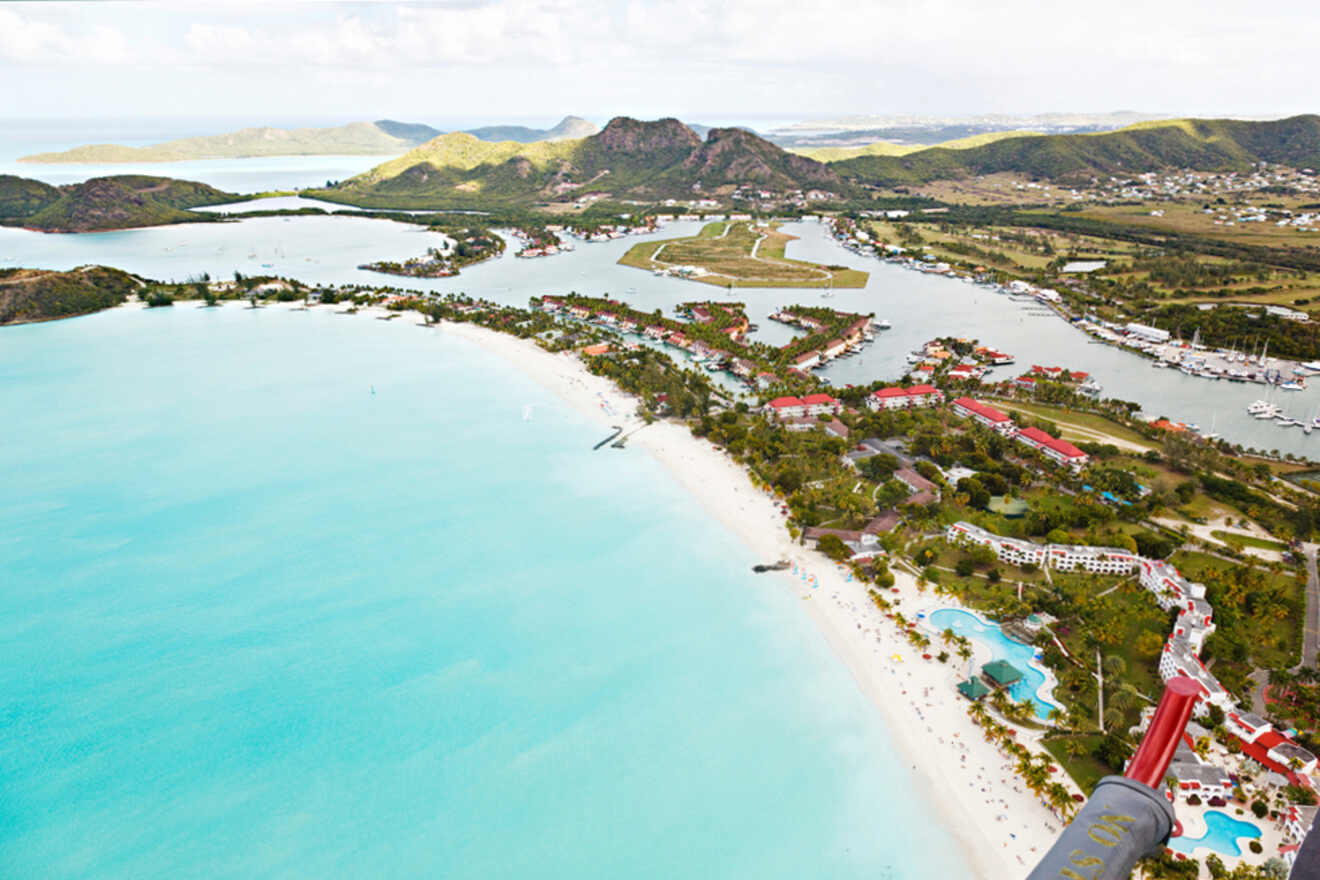 Aerial view of a tropical coastline with clear turquoise waters, white sandy beaches, lush greenery, and developed areas near a bay.