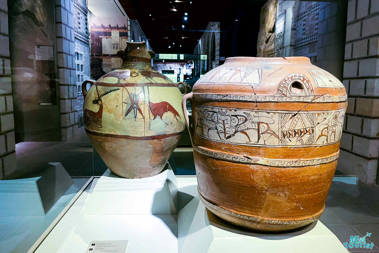 Antique Anatolian ceramics displayed in a museum, including two large pots with intricate designs and inscriptions