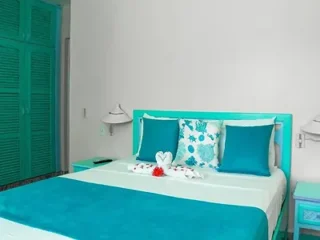 A bright tropical-themed bedroom with turquoise bedding, white furniture, and green shutters.