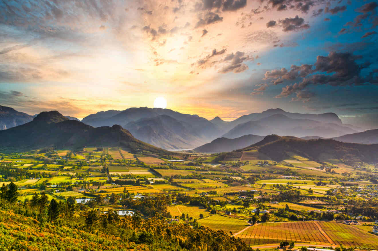 Breathtaking sunset view over the Franschhoek wine region with the sun casting a warm glow on the vineyard-covered valleys and distant mountains.