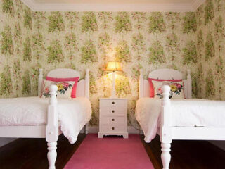 A charming bedroom with two single white beds set against a floral wallpaper backdrop