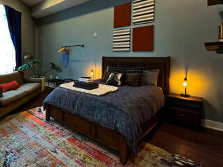 A spacious guest room with eclectic furnishings, a comfortable bed with dark bedding, lit by warm lamps