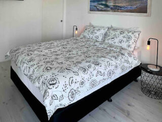 Bedroom with a cozy bed with black and white floral bedding and a sea-scape picture above the bed