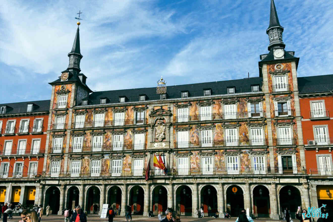 The vibrant Plaza Mayor of Madrid, showcasing the richly decorated façade of the Casa de la Panadería and people strolling across the historical square.