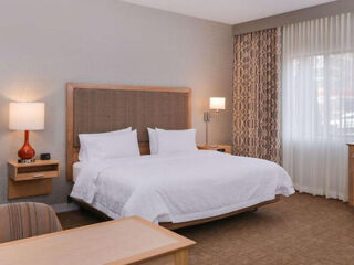 Hotel room featuring a large bed with a tan headboard, coordinated drapery, and contemporary furniture