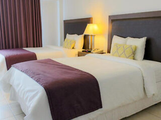 Welcoming hotel bedroom with two queen beds, maroon throws, and warm bedside lighting