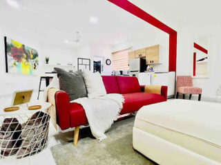 A spacious, red-accented living area with a large sofa, modern art, and an open kitchen layout.
