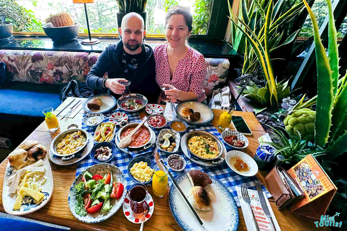 the author of the post with her husband toasting over a table full of various Turkish breakfast dishes in a vibrant restaurant setting