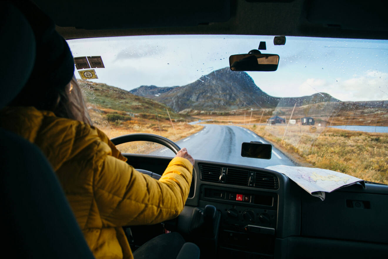 Inside view of a car with a female driver at the wheel, traveling on a remote road with a map on the dashboard, evoking the freedom of a road trip through Ireland's rugged terrain.