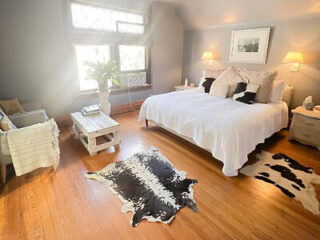 Spacious and rustic bedroom with a queen-sized bed, hardwood floors, and a faux cowhide rug
