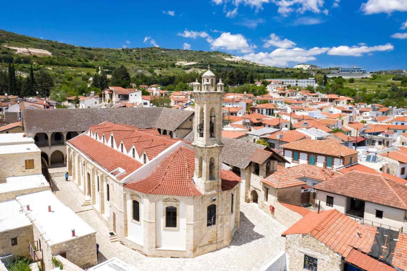 Aerial view of Omodos Village, featuring the historic monastery with its prominent bell tower, surrounded by traditional red-roofed houses and green hills