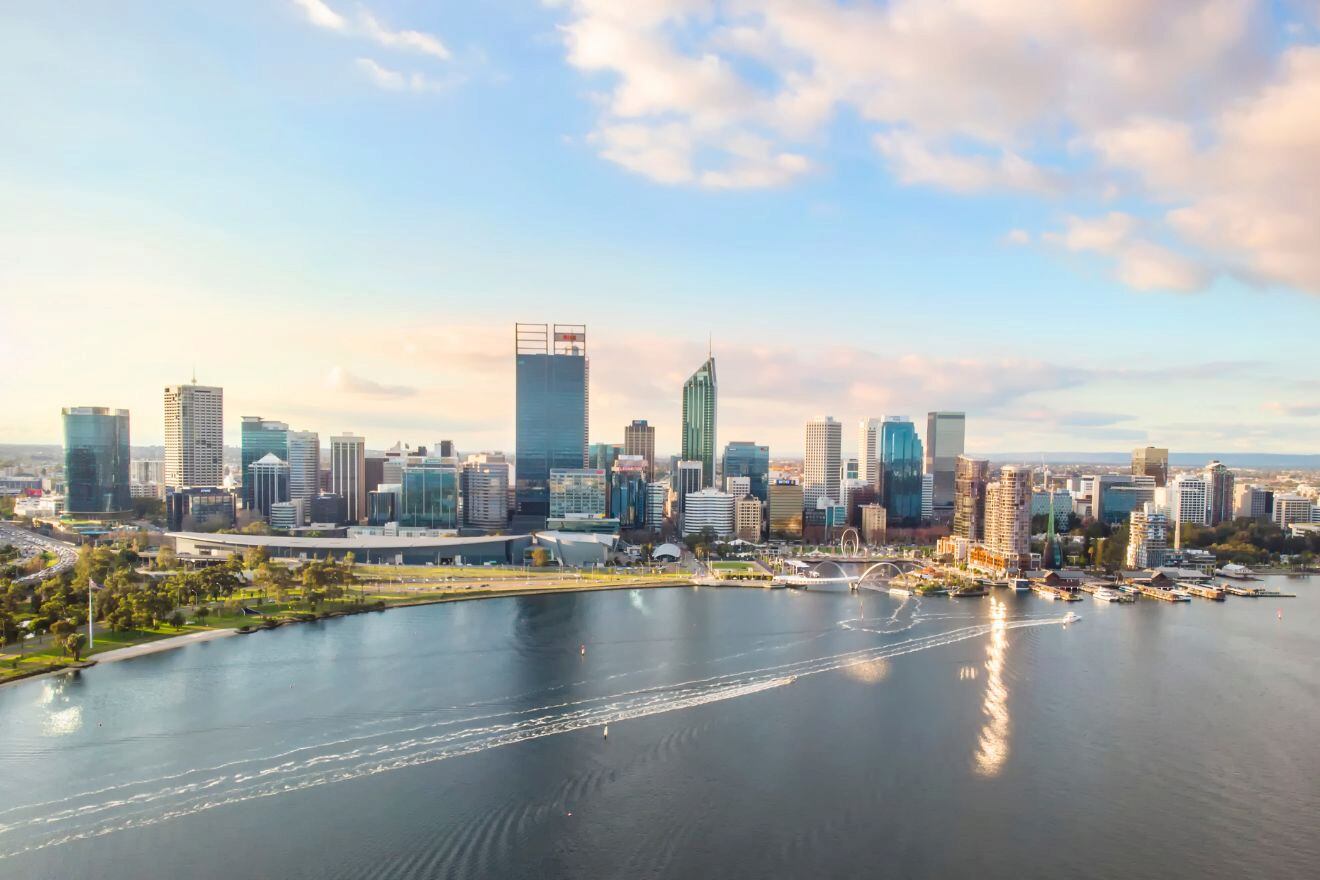 Aerial view of a modern city skyline of Perth at sunset with waterfront buildings and scattered clouds.