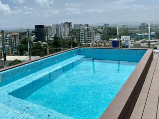 Piscina na cobertura com água azul cristalina e vista para a paisagem urbana com prédios altos sob um céu parcialmente nublado.
