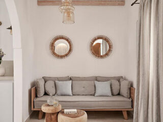 A neutral-toned living room with a light gray sofa, two round wooden mirrors above it, small round wooden side tables, and sheer curtains.