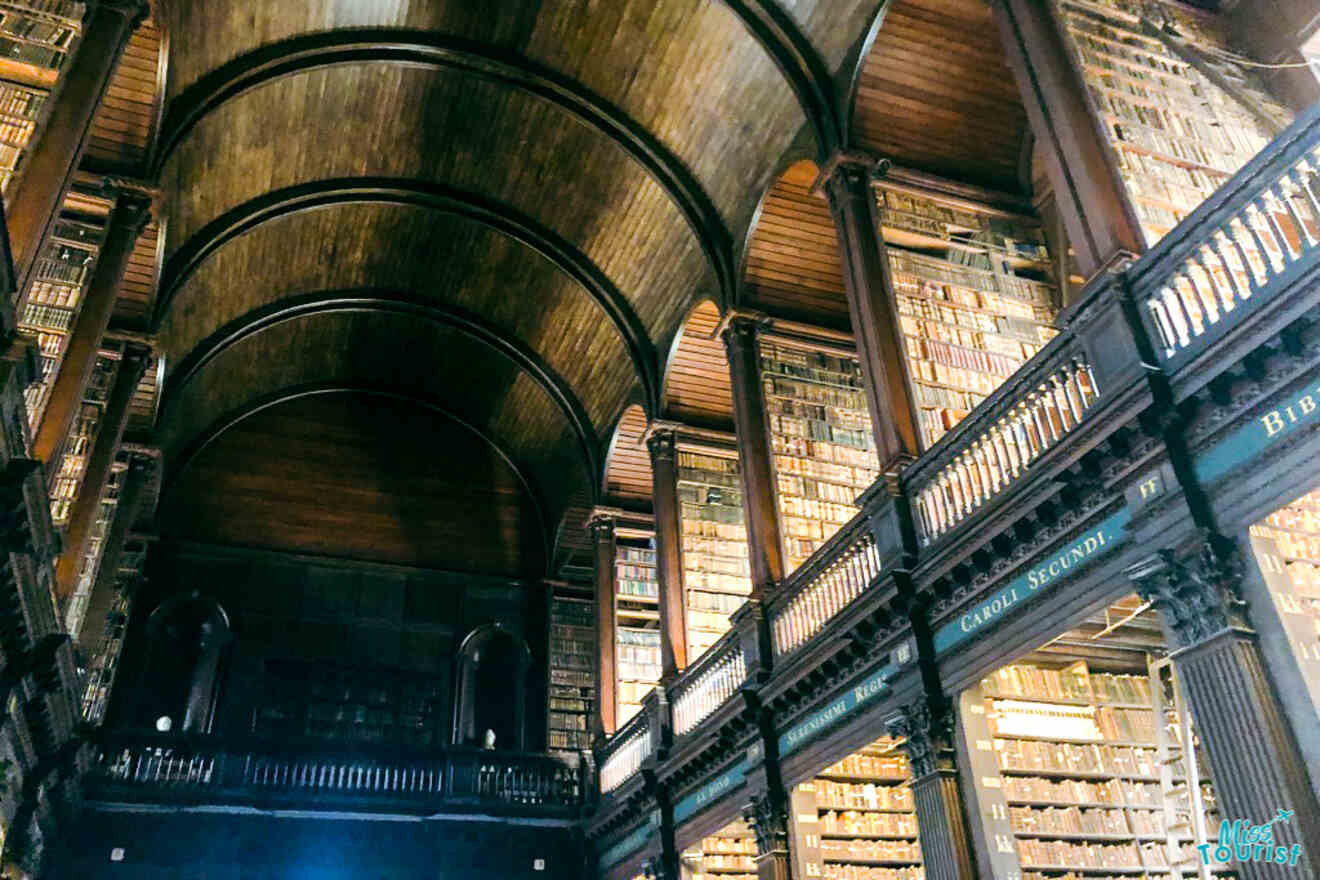 The Long Room of the Trinity College Library in Dublin, showcasing the vast collection of ancient books lined in wooden shelves, with bust statues and a vaulted ceiling.