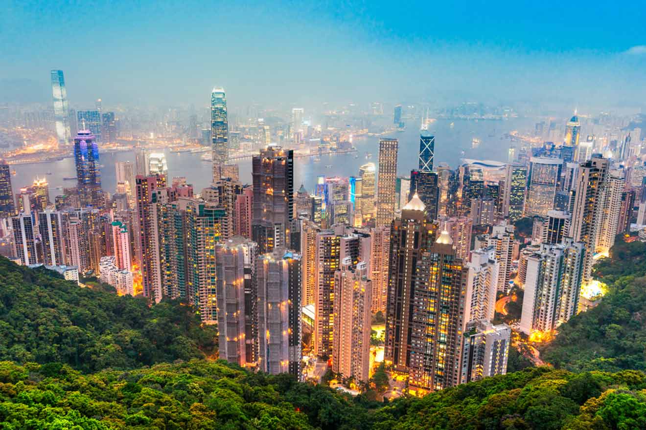 A panoramic view of Hong Kong's skyline with towering skyscrapers illuminated at dusk against a vibrant sunset sky, showcasing the city's dense urban architecture.