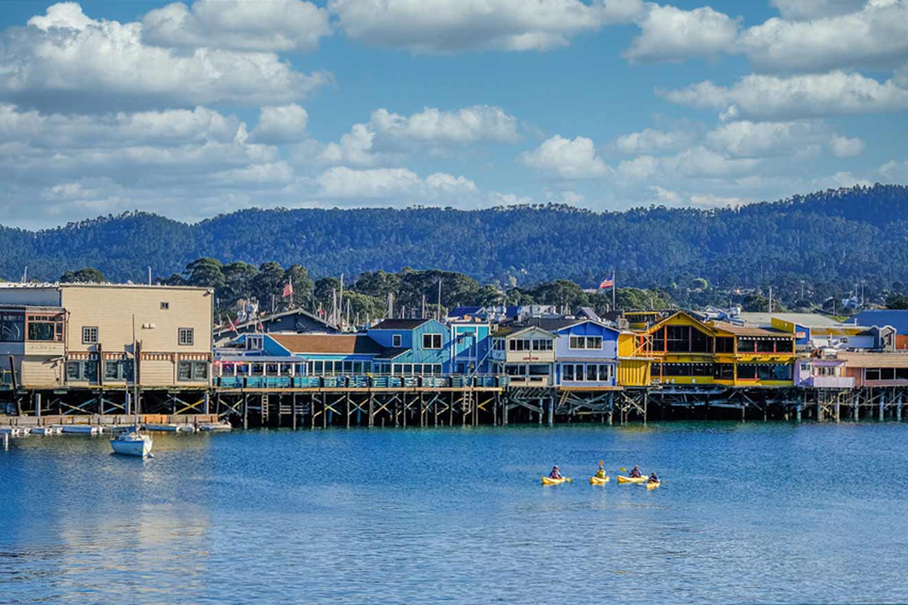 Colorful buildings on a pier with mountains in the background, people kayaking on calm water in the foreground.
