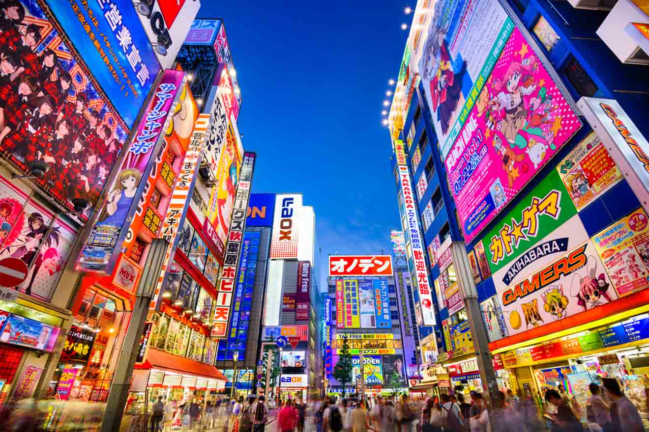 Bustling night scene at Akihabara district in Tokyo with bright neon signs and billboards displaying anime and electronics advertisements, as a blurred crowd walks through the vibrant streets.
