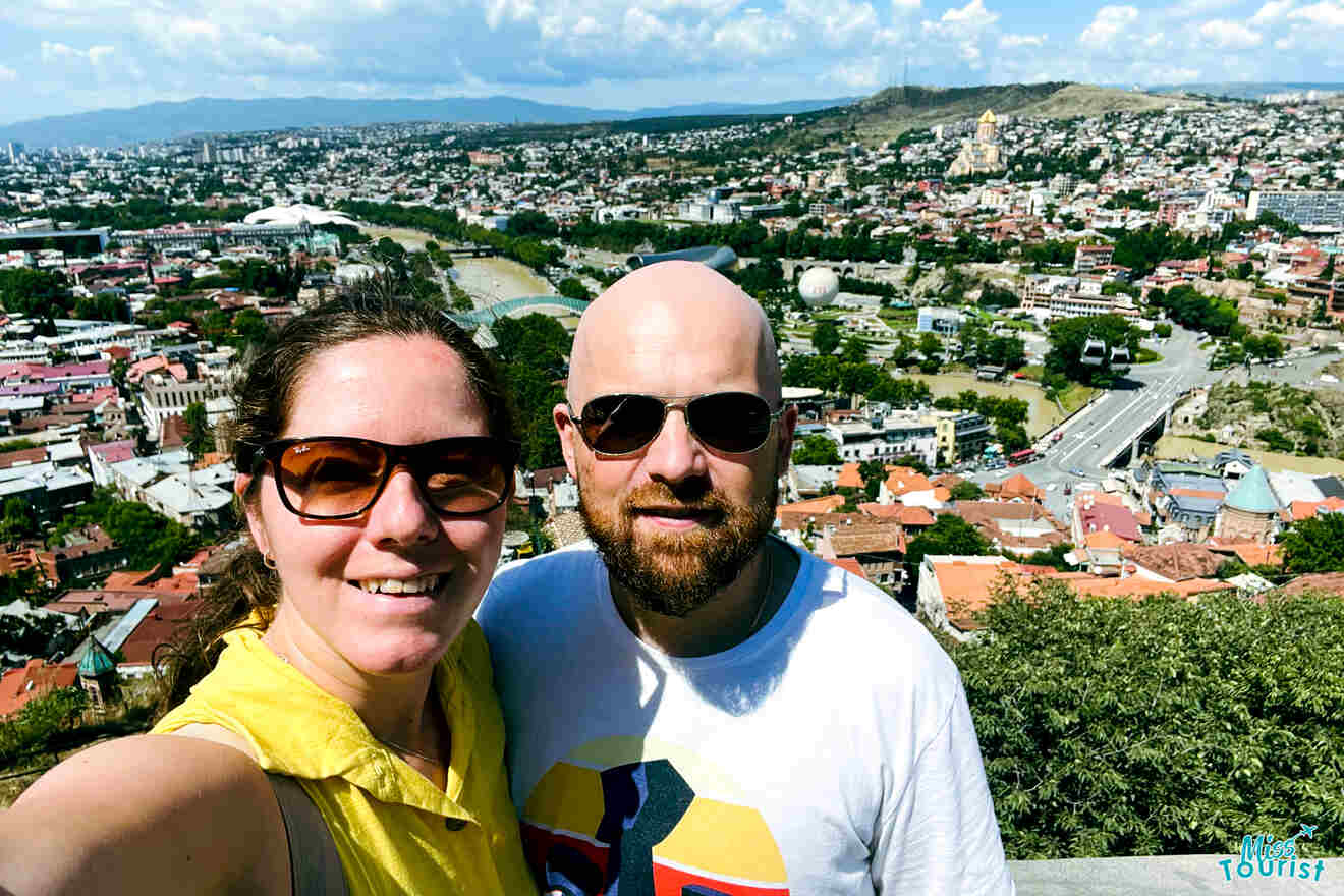 A selfie of a the writer of the post and her partner with the panorama of Tbilisi in the background, highlighting a personal travel experience against a cityscape.