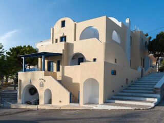A beige, multi-level building with curved and arched architectural features stands beside a set of white stairs under a clear blue sky.