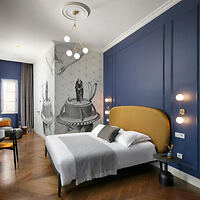 A modern bedroom with a blue accent wall, a yellow upholstered bed, and a mural depicting classic sculptures. The room features wooden flooring, contemporary lighting, and a seating area.
