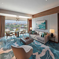 A luxurious hotel suite featuring elegant decor with a blue and beige color scheme, a seating area, and a view of the city.