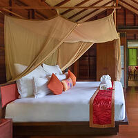 A luxurious bed with a canopy, colorful pillows, and elegant decor in a tropical bungalow.