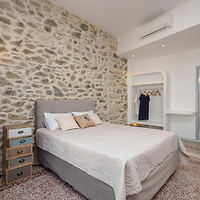 A cozy bedroom featuring a stone accent wall, a comfortable double bed with neutral bedding, and an open closet space with minimalistic decor.