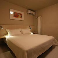 A cozy and minimalist hotel room with a comfortable bed, bedside lamps, and a colorful painting above the headboard.