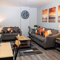 A cozy living room in Stay Pittsburgh, featuring modern furniture, vibrant orange accents, and a large wall clock