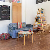 A cozy common area featuring a blue couch, a small table, a chalkboard, and a shelf with books and games.