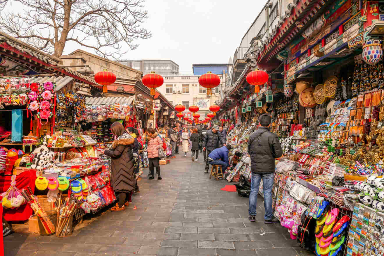 A lively market street in Wangfujing filled with colorful stalls, red lanterns, and people shopping for souvenirs.