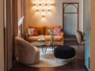 A stylish living area with a brown sofa, modern chairs, a round coffee table, and unique wall lighting in a cozy, well-decorated room.
