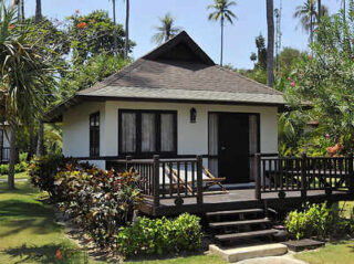 A charming bungalow surrounded by lush greenery and tall palm trees.