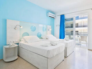 A twin bedroom with white beds and blue accents, featuring a balcony with a view.
