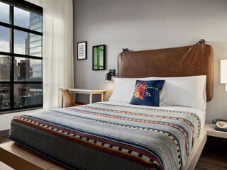 A stylish hotel room with a large bed, city views from the window, and modern decor.