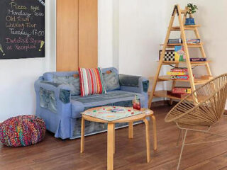 A cozy common area with a blue couch, a small table, a chalkboard, and a ladder shelf with books and games