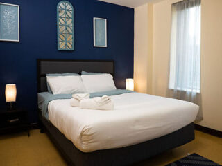 A cozy bedroom with a dark blue accent wall, featuring a neatly made bed and minimalist decor.