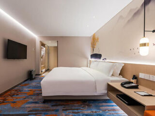 A modern hotel room with a large bed, a wall-mounted TV, and a stylishly decorated wall.