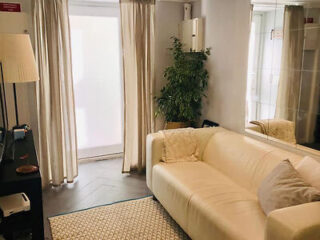 A small living area with a white couch, potted plant, and natural light filtering through sheer curtains