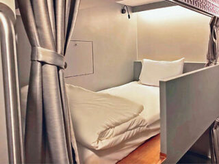 A compact sleeping pod with a privacy curtain and comfortable bedding.